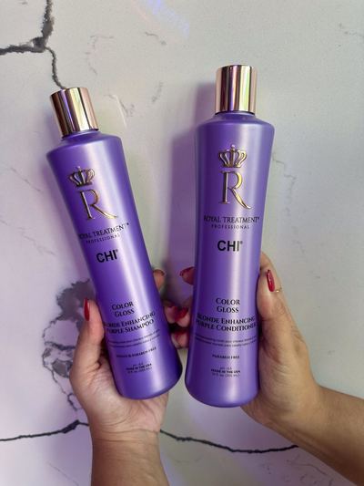 Zwei violette CHI Royal Treatment Color Gloss Flaschen werden vor einer hellen Marmorwand in zwei Händen gehalten.
