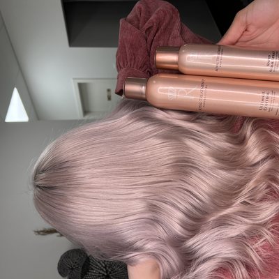 Zwei roségoldene Flaschen der Reihe CHI Royal Treatment, in einer Hand über hell rosé gefärbtem, gewelltem Haar gehalten.