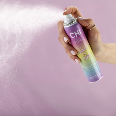Eine Hand hält eine bunte CHI Vibes Sprühdose und sprüht eine feine Wolke vor rosa Hintergrund.